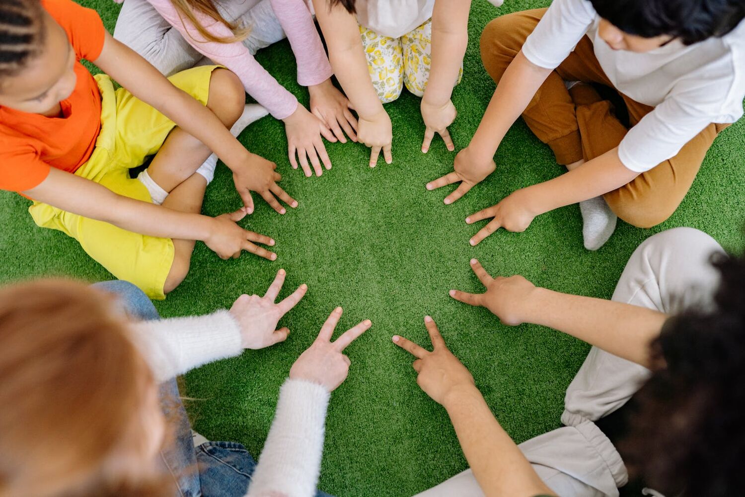 een groep kinderen zitten in een cirkel en steken een vier op met hun vinger.