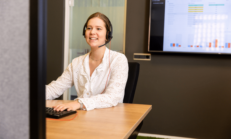 Vrouw in wit shirt met headset zit achter computer te werken