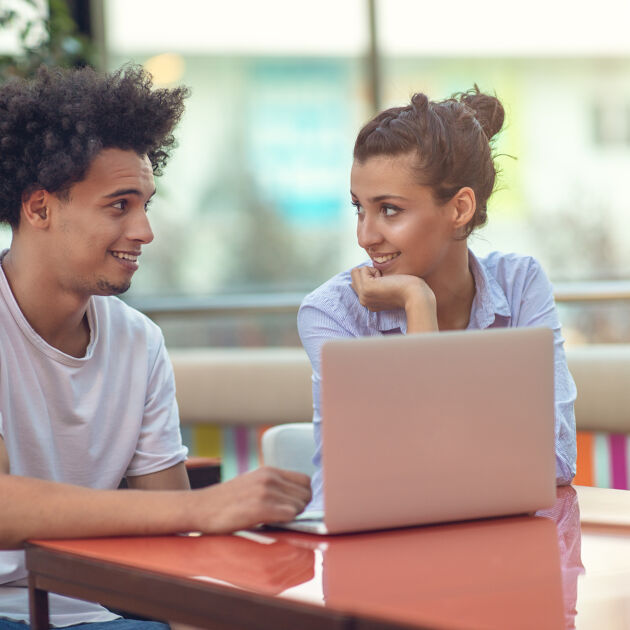 Man en vrouw kijken naar elkaar achter laptop. 