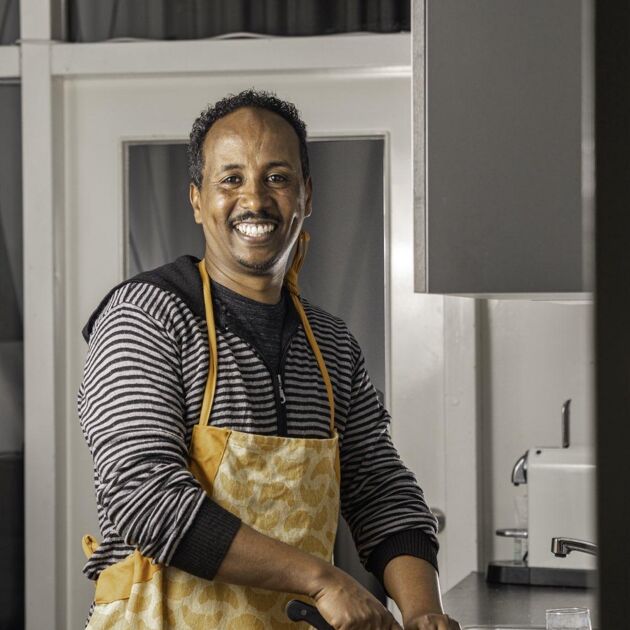 Man in schort snijdt groente op houten plank in keuken