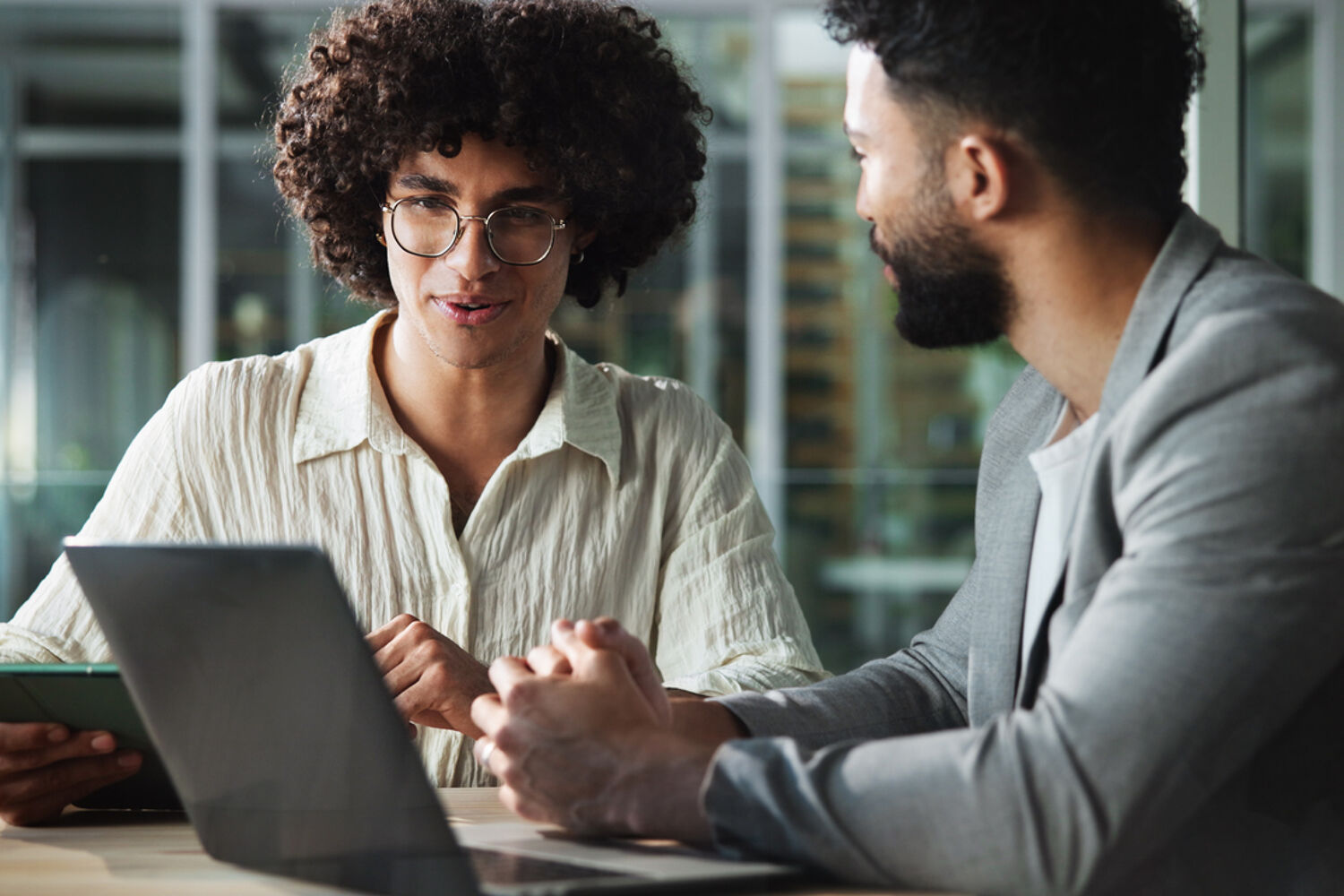 Twee mannen zitten aan bureau, een man kijkt naar de laptop, ander man kijkt naar man.