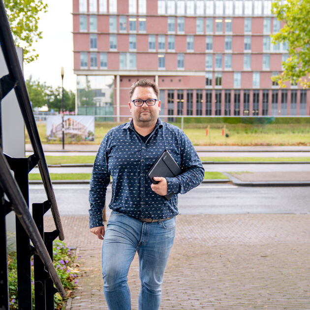 Man in blauw shirt en met bril loopt buiten een trap op met een iPad in zijn handen.