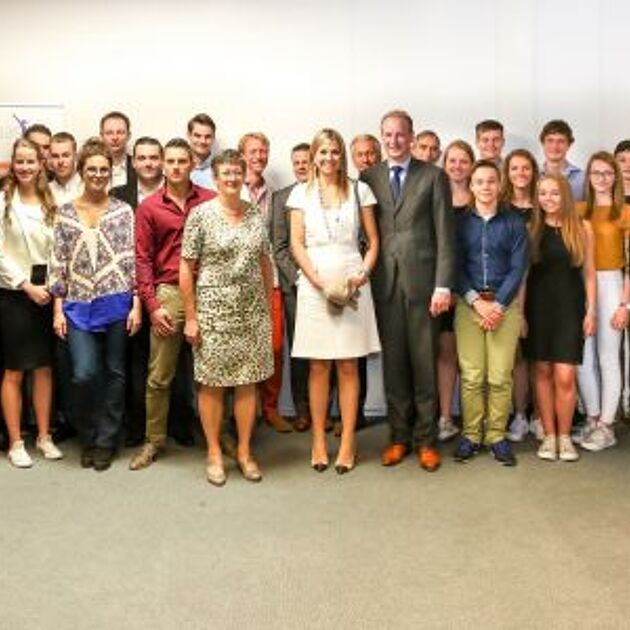 Een grote groep mensen staan voor een witte muur