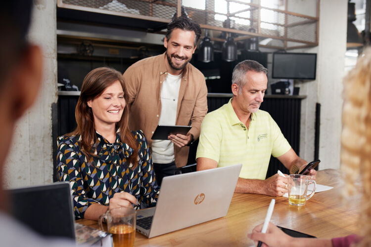 Drie mensen zitten aan een tafel en werken met laptop en tablet.
