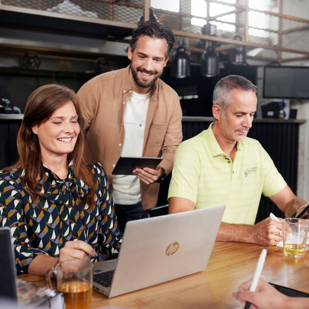 Drie mensen zitten aan een tafel en werken met laptop en tablet.