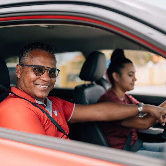 Man in rood shirt en zonnebril geeft auto rijles aan vrouw