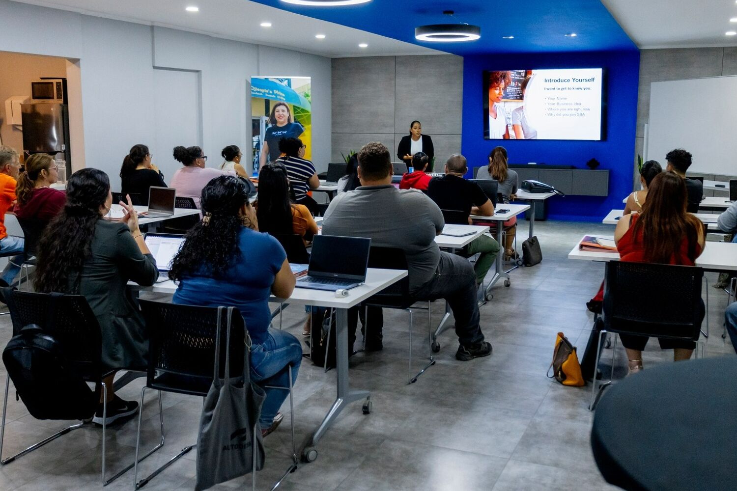 Small-Business-Academy-klaslokaal Een zaal met mensen ingericht als een schoollokaal. Er zijn mensen die een presentatie geven