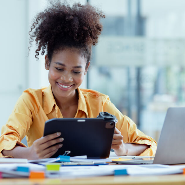 Lachende vrouw met gele blouse kijkt naar tablet. 