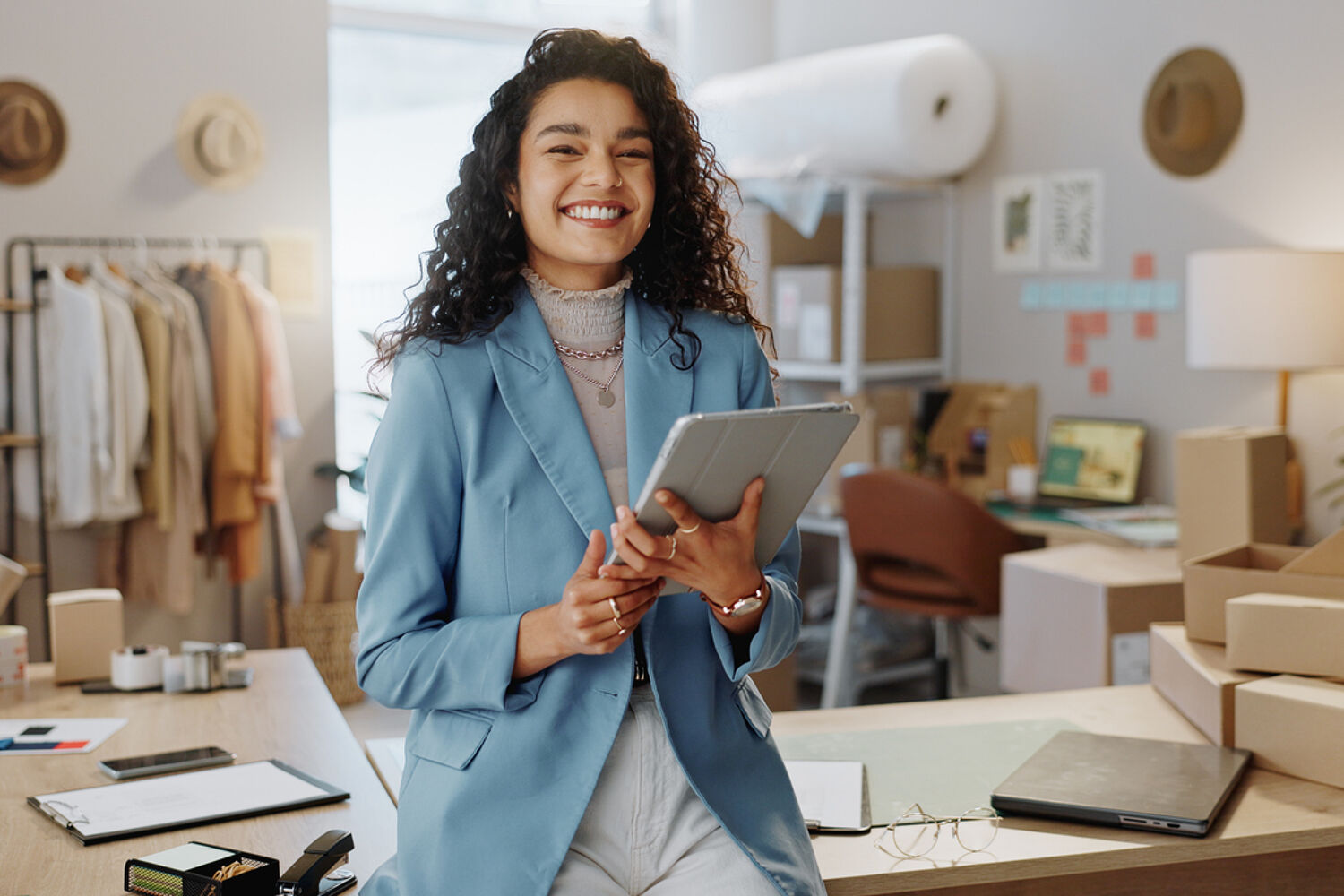 vrouw-met-Ipad-in-de-hand-lacht-in-camera-zit-op-bureau Vrouw met Ipad in de hand lacht in camera zit op bureau