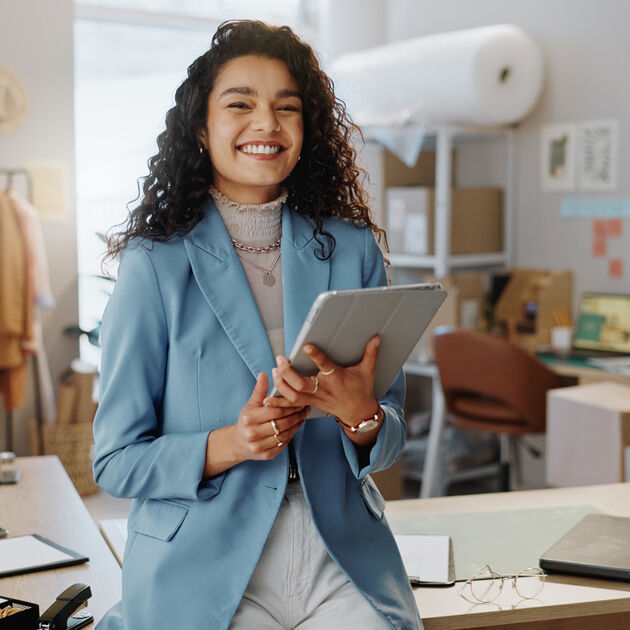 Vrouw met Ipad in de hand lacht in camera zit op bureau
