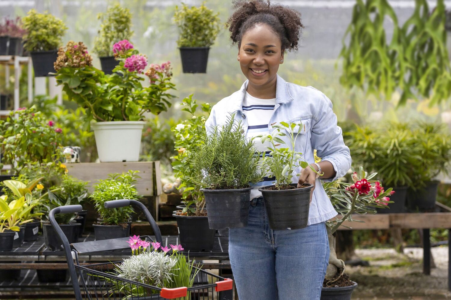 Vrouw kijkt lachend en staat buiten met twee planten in haar hand. 