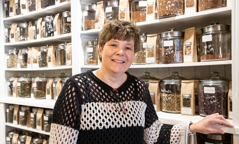 Vrouw in wit zwart shirt staat voor muur van thee