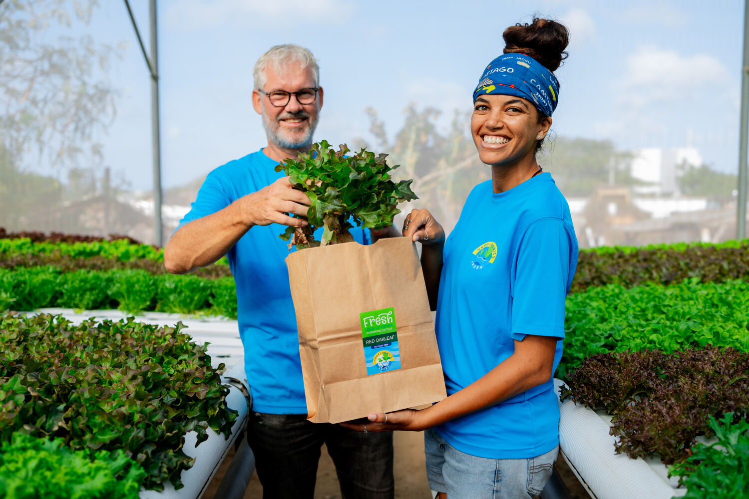 Man-en-vrouw-houden-plant-vast-blauw-shirt Man en vrouw in blauwe werk shirts verpakken groenten buiten