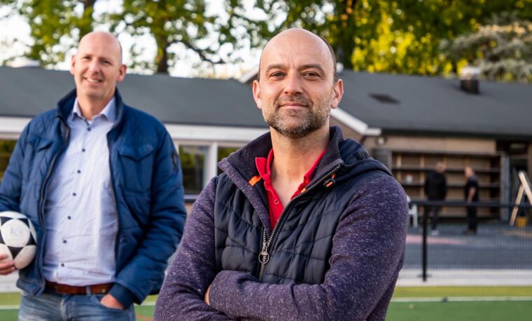 man lacht naar camera met andere man op achtergrond 
