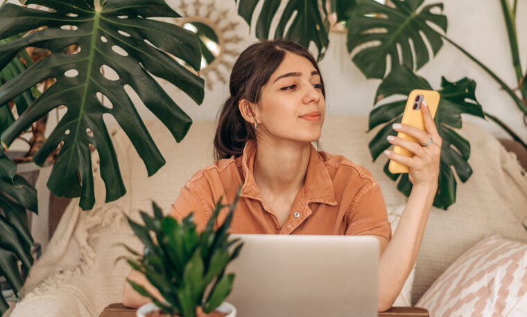 Vrouw zit achter de laptop en kijkt naar haar telefoon met veel planten