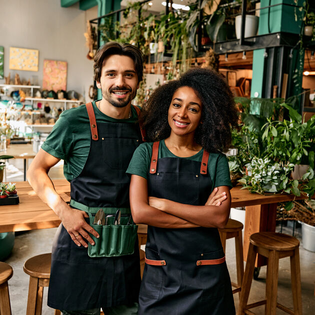 Man en vrouw met schort om staan trots in een plantenwinkel. 