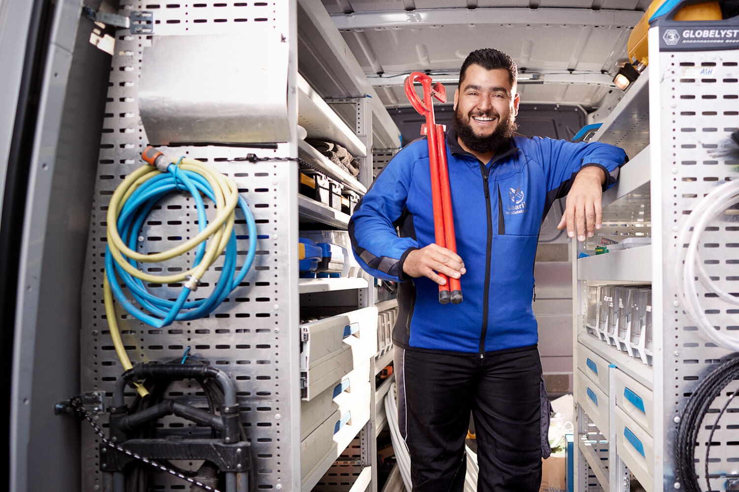 Man met een blauwe jas staat lachend in een werkbus.