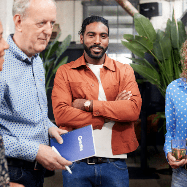 Man in oranje jasje kijkt naar de camera met mensen om zich heen