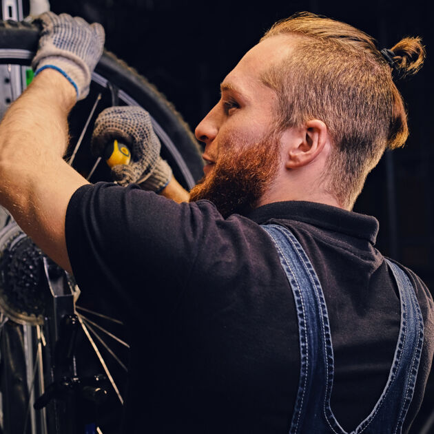 Een lachende man met een knot en overall sleutelt aan een fiets. 