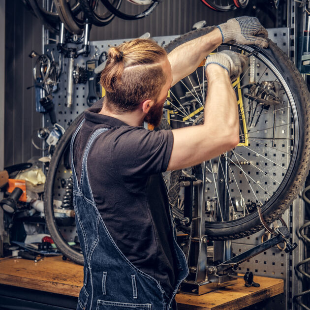 Een man met een overall aan sleutelt aan een wiel van een fiets. 