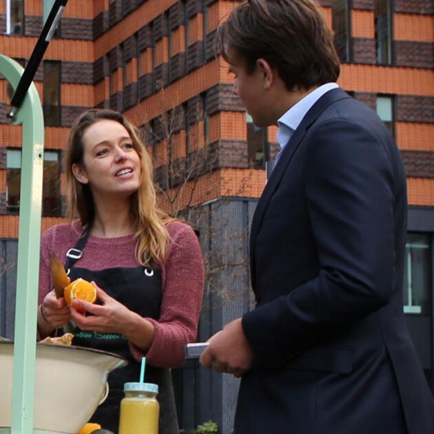 Vrouw en man zijn aan het praten, bij haar kraampje waar ze verse fruit drankjes maakt