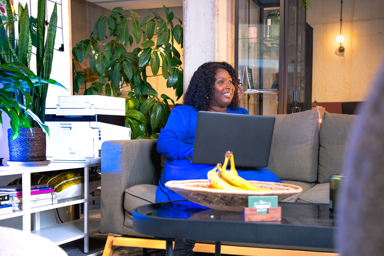 Traienne-trai-vegan-hulp-van-qredits vrouw met blauwe jurk zit op de bank met haar laptop