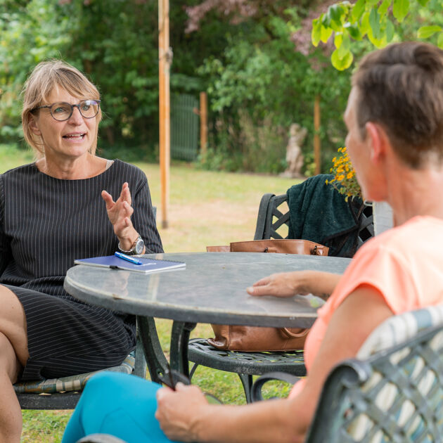 Twee vrouwen zitten aan tafel en zijn in gesprek.