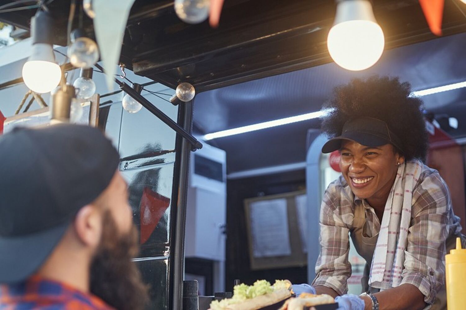 Vrouw lacht en staat in foodtruck en geeft eten aan de klant.