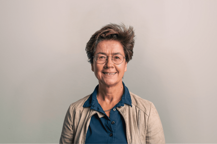 Conny medewerker Qredits vrouw in bruin jasje voor grijze achtergrond