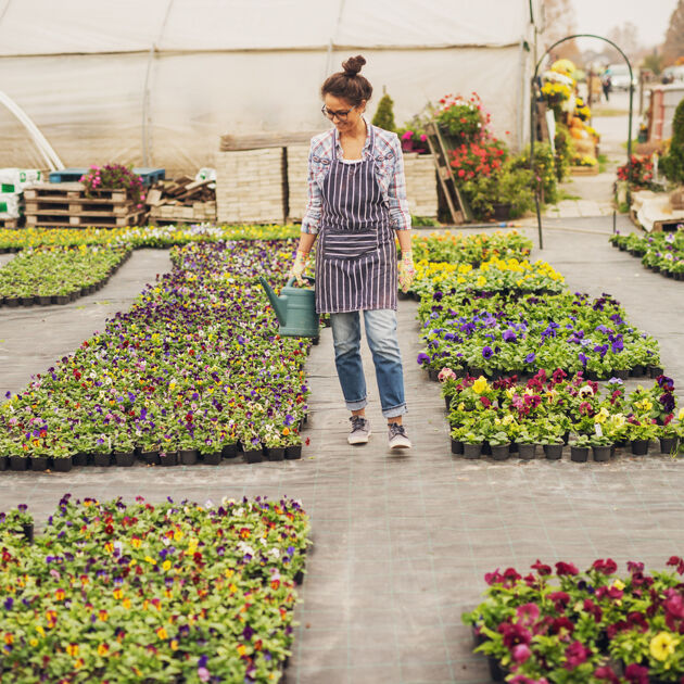 vrouw kijkt naar bloemen in een kas en loopt rond met een gieter