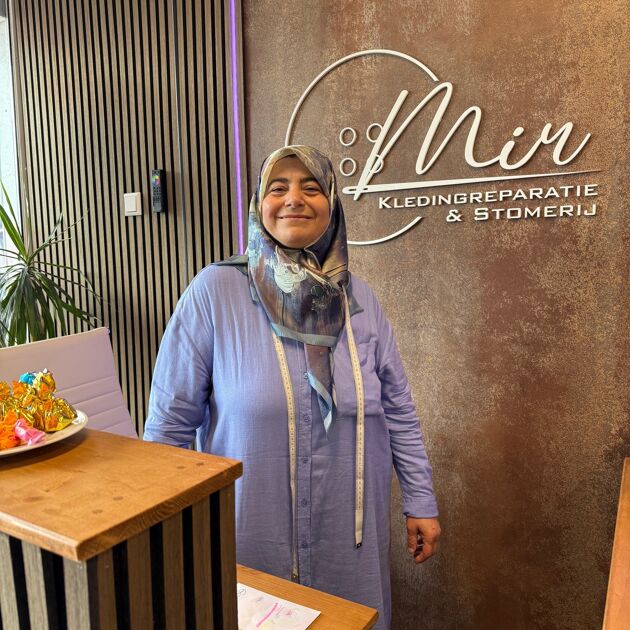 Lachende vrouw met een blauwe blouse aan staat bij de balie. 