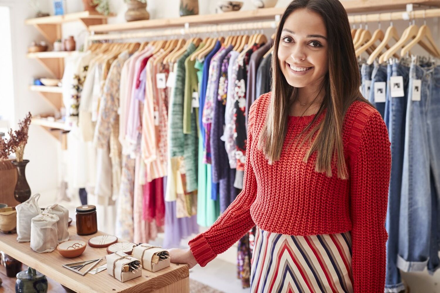Vrouw staat in een kledingwinkel en leunt op balie, ze lacht. 