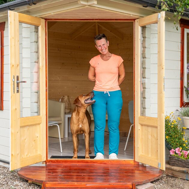 Een lachende vrouw staat in een deuropening met een bruine hond naast haar.