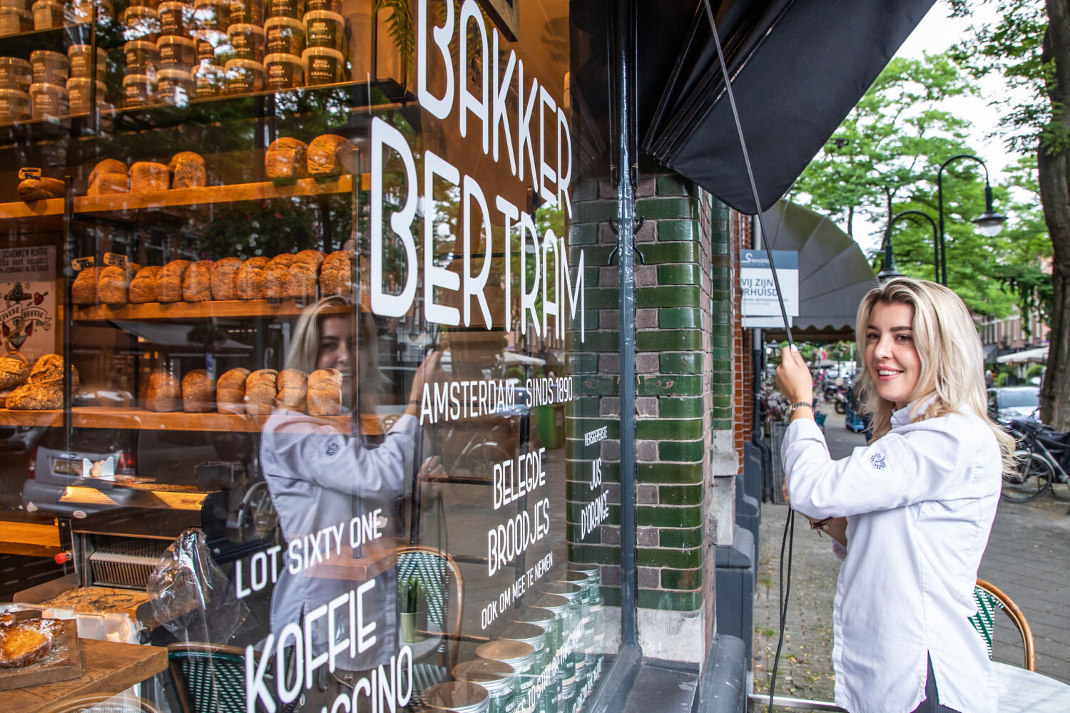 Vrouw opent ontvouwd het zonnescherm van haar bakkerij.