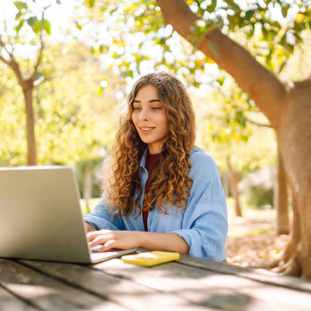 Vrouw zit buiten en werkt achter laptop. 