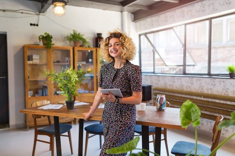 vrouw-krullend-haar-staat-voor-bureau-ipad-in-hand