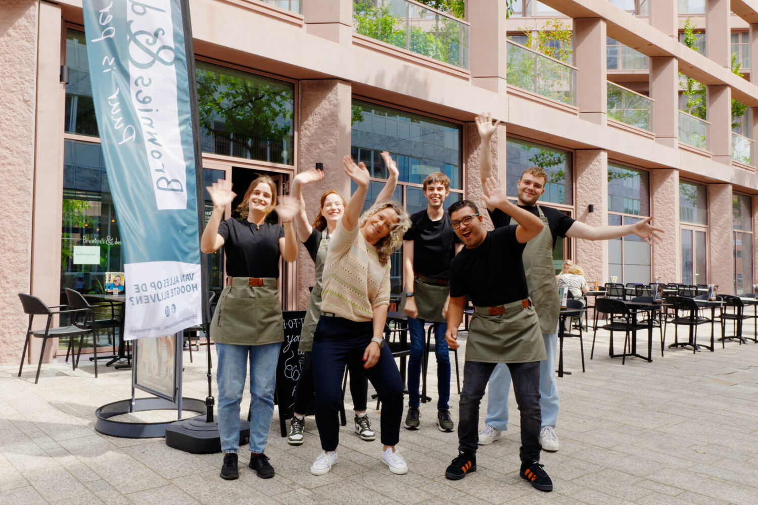 Een groep mensen staan buiten en zwaaien naar de camera.