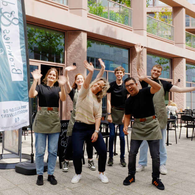 Een groep mensen staan buiten en zwaaien naar de camera.