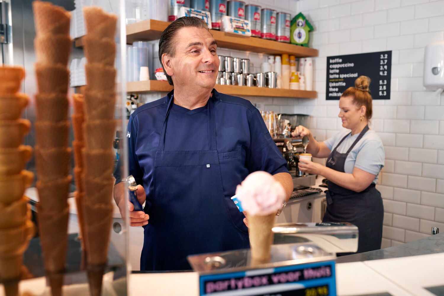 Lachende man met blauw schort aan het werk in een ijssalon. 