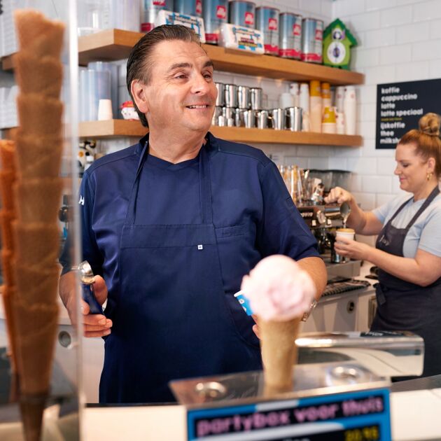 Lachende man met blauw schort aan het werk in een ijssalon. 
