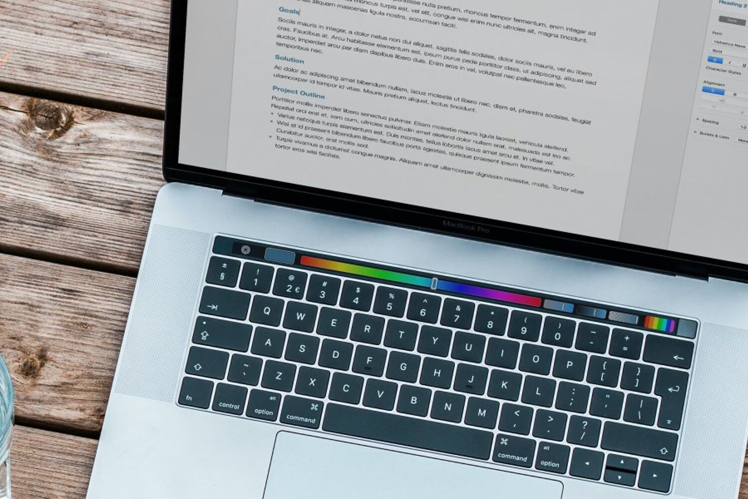 een laptop omringt met een glas water, kladblok en telefoon staan op een tafel