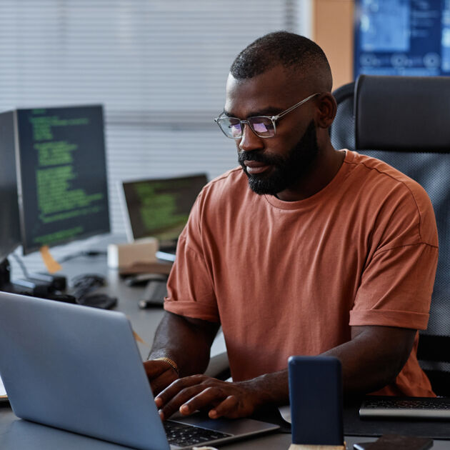Man met bril zit aan bureau achter laptop.
