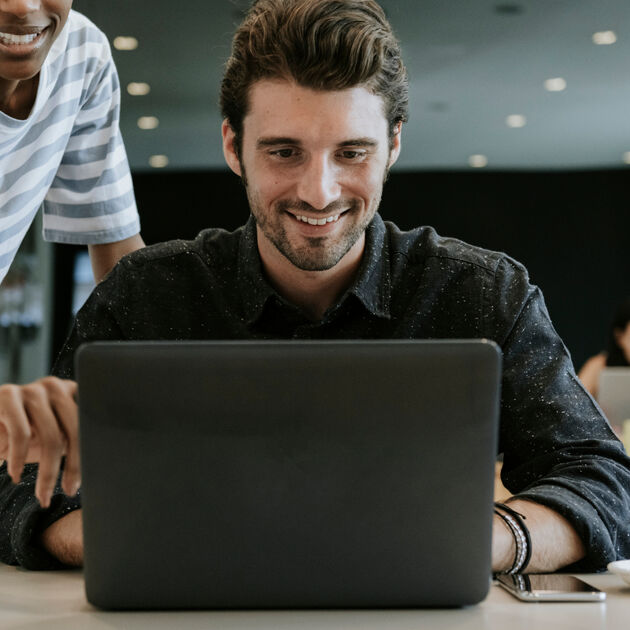 Man zit achter laptop met kopje, vrouw wijst naar laptop.
