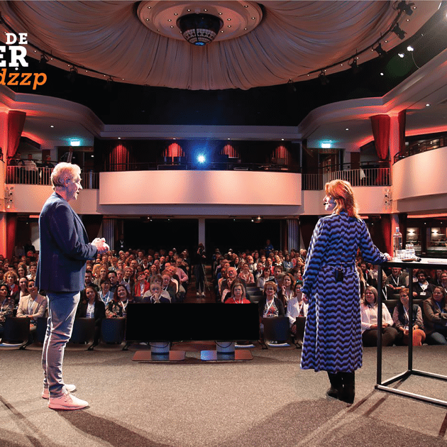 Man en vrouw staan op podium voor een zaal mensen