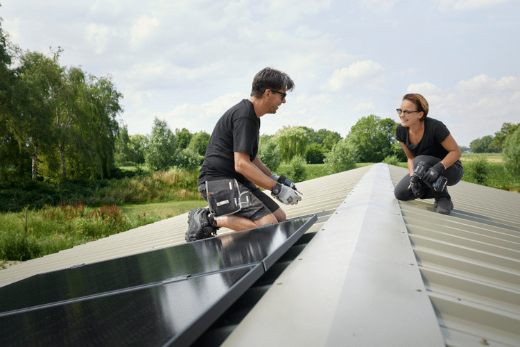 man-en-vrouw-werken-op-dak-van-schuur-zonnepanelen