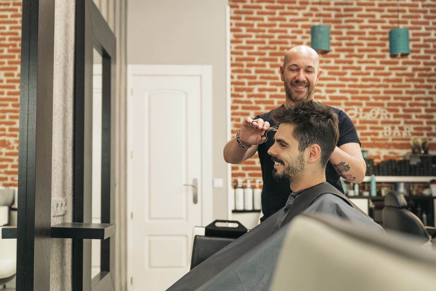 Man met zwart shirt knipt een andere man met donker haar. 