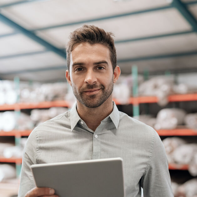 Lachende man met een blouse aan en tablet in zijn handen staat in een hal. 