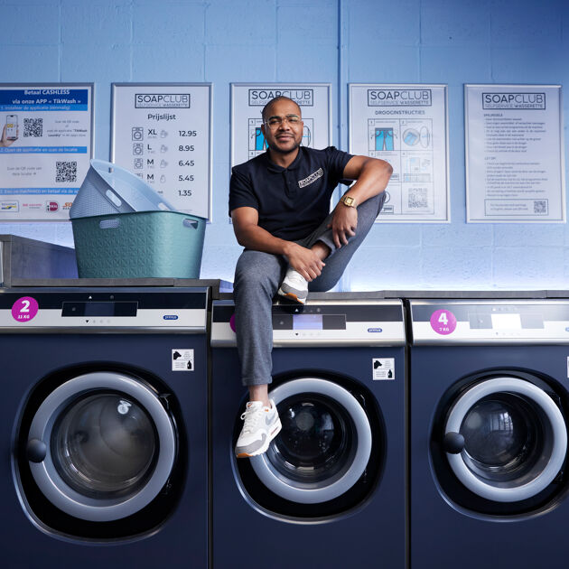 Een man zit op wasmachines met wasmanden naast hem. 