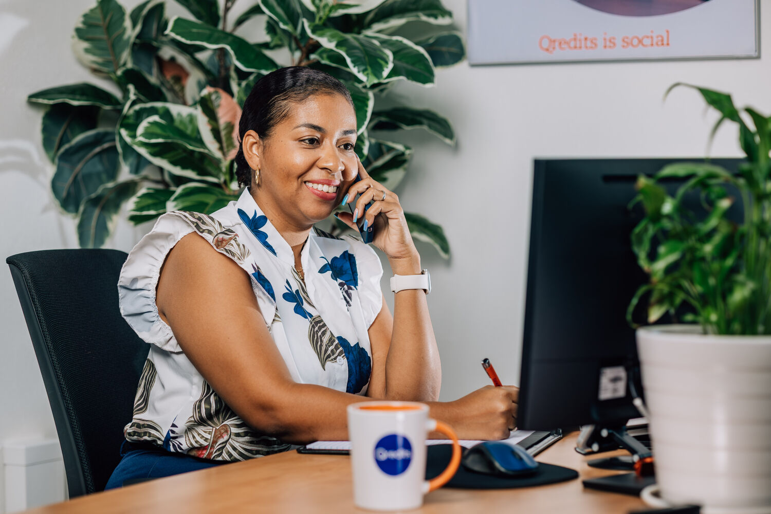 medewerker-qredits-telefoon-lach- Vrouw schrijft en belt achter haar computer.