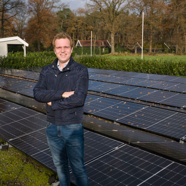 Man in jas staat buiten voor een veld zonnepanelen. 